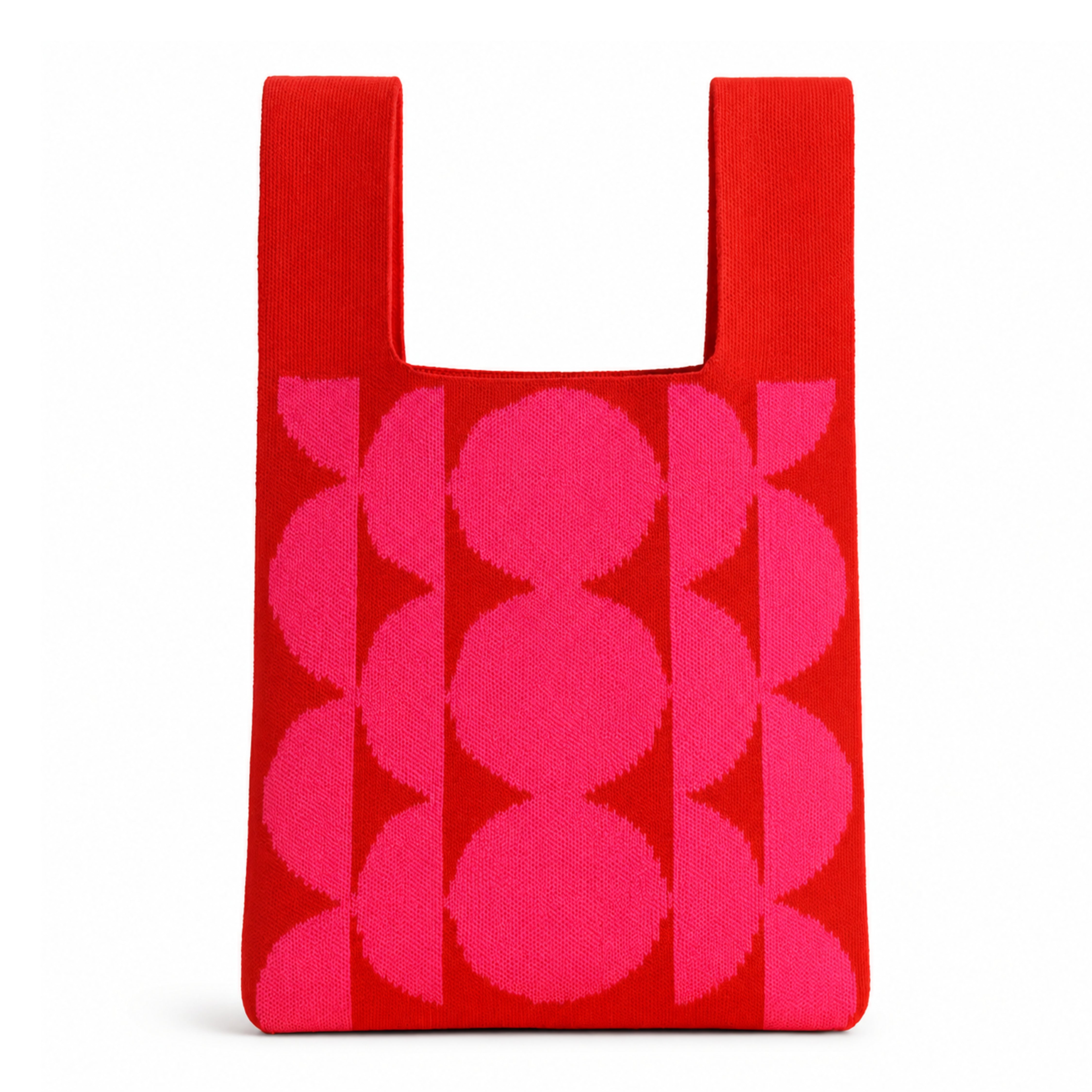 Bright red knitted tote bag featuring a bold hot pink geometric pattern of oversized circles and semi-circles. Shown standing upright against a clean white background with soft natural shadows, highlighting the knitted texture, structured silhouette and contemporary Scandinavian-inspired design.