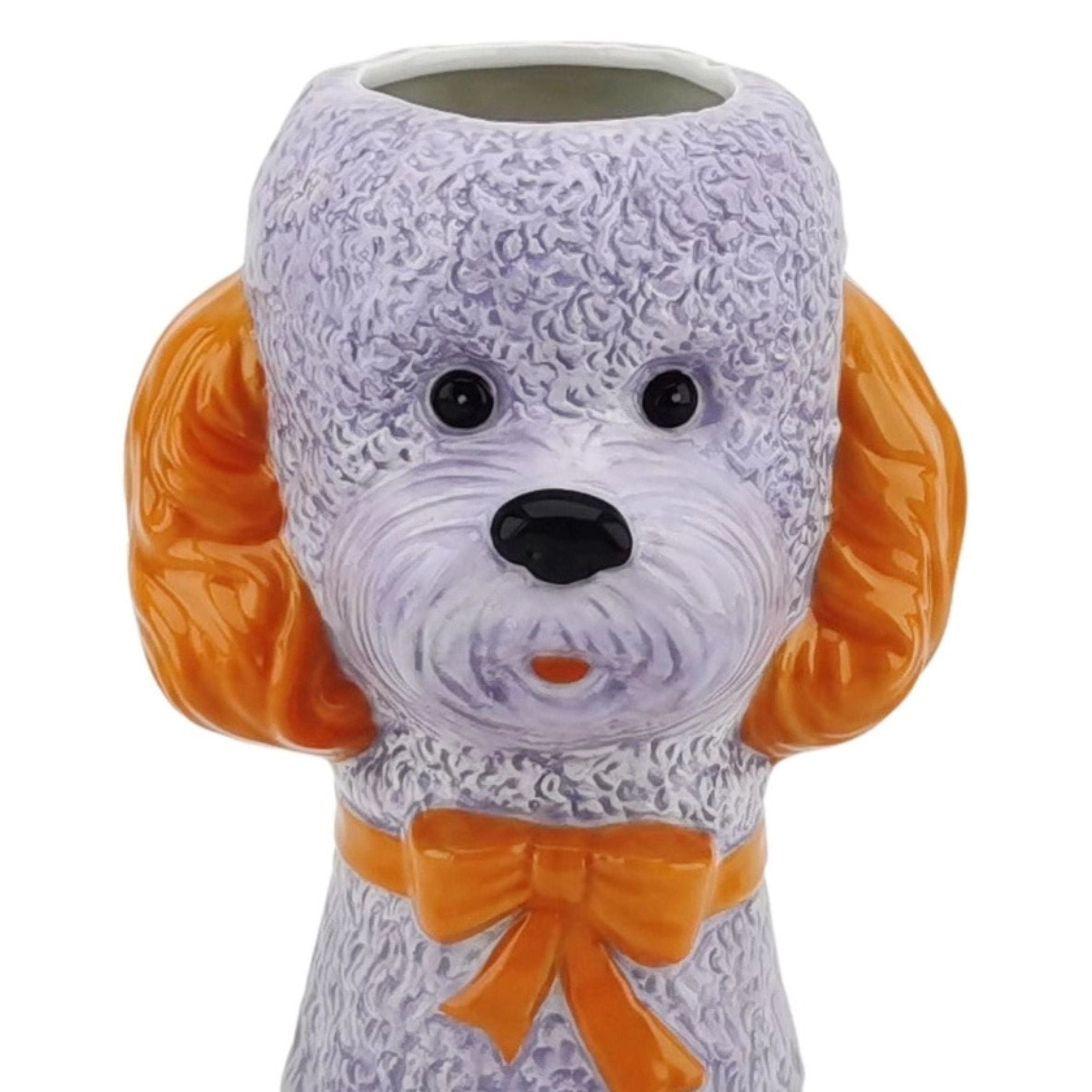 Close-up of a lilac dog-shaped ceramic vase with orange ears and an orange bow on a white background.