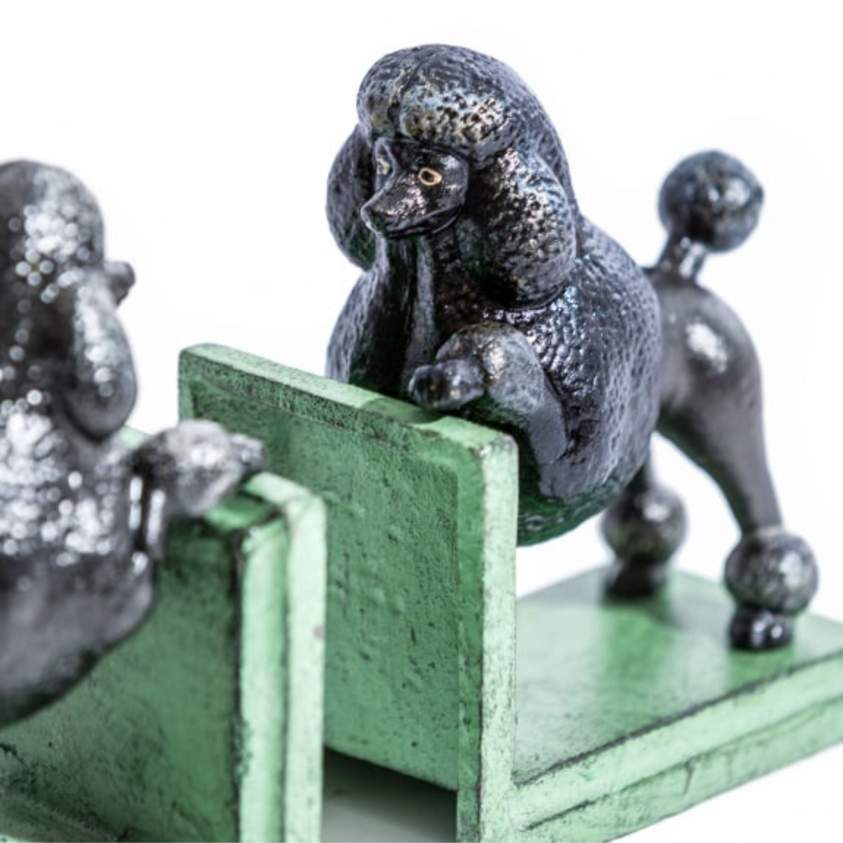 Close-up of black cast iron poodle bookends with vintage green bases, highlighting detailed texture and playful pose on a white background.