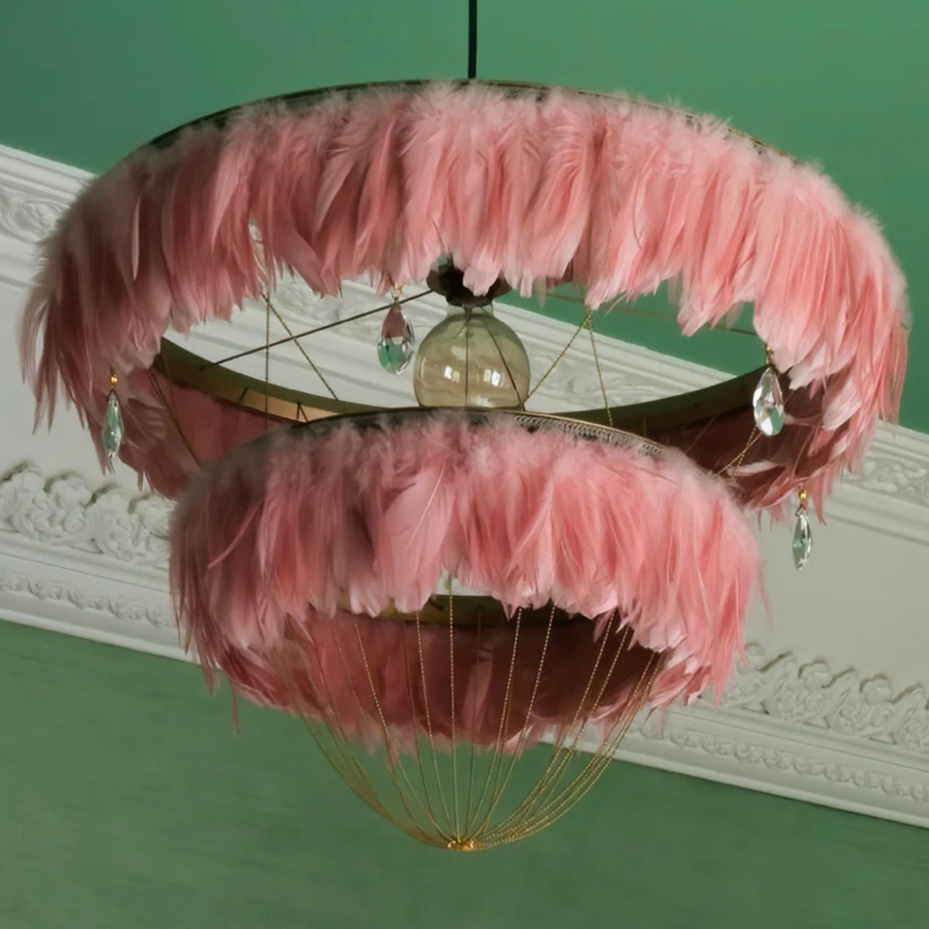 Flamingo pink two-tier Bertie feather light shade with crystal drops, hanging against a green wall with white ceiling moulding