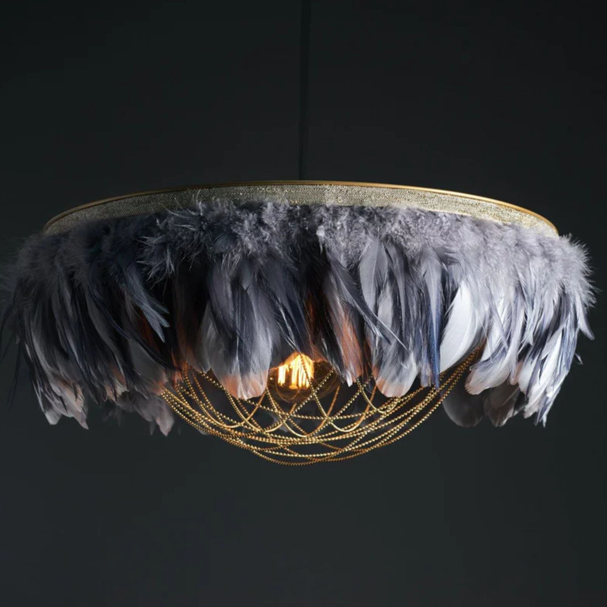 Gloria two-tone grey feather light shade with brass ball-chain trim, illuminated pendant against a dark background.