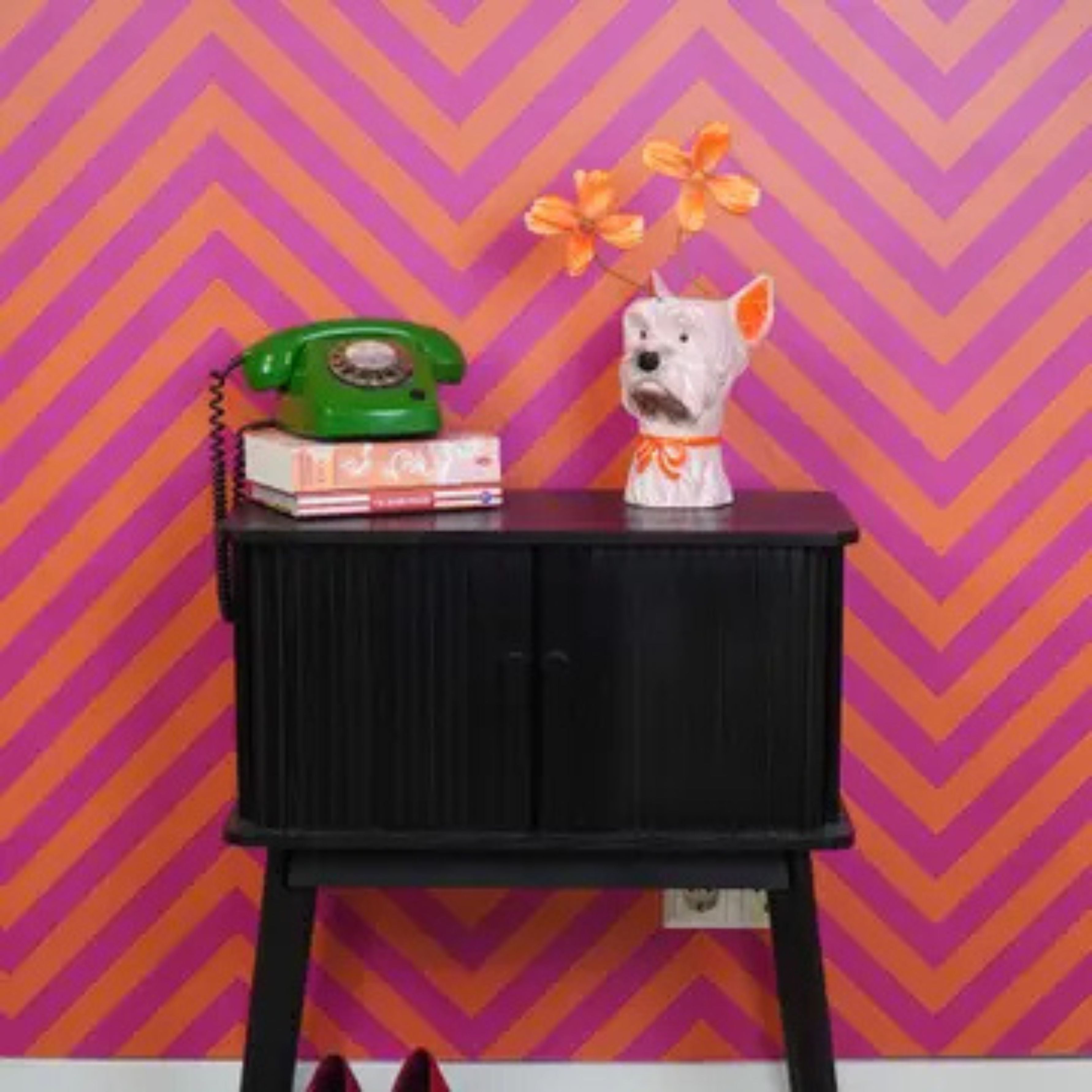 Pink and orange dog-shaped ceramic vase on a black cabinet with retro decor in front of a vibrant chevron wallpaper