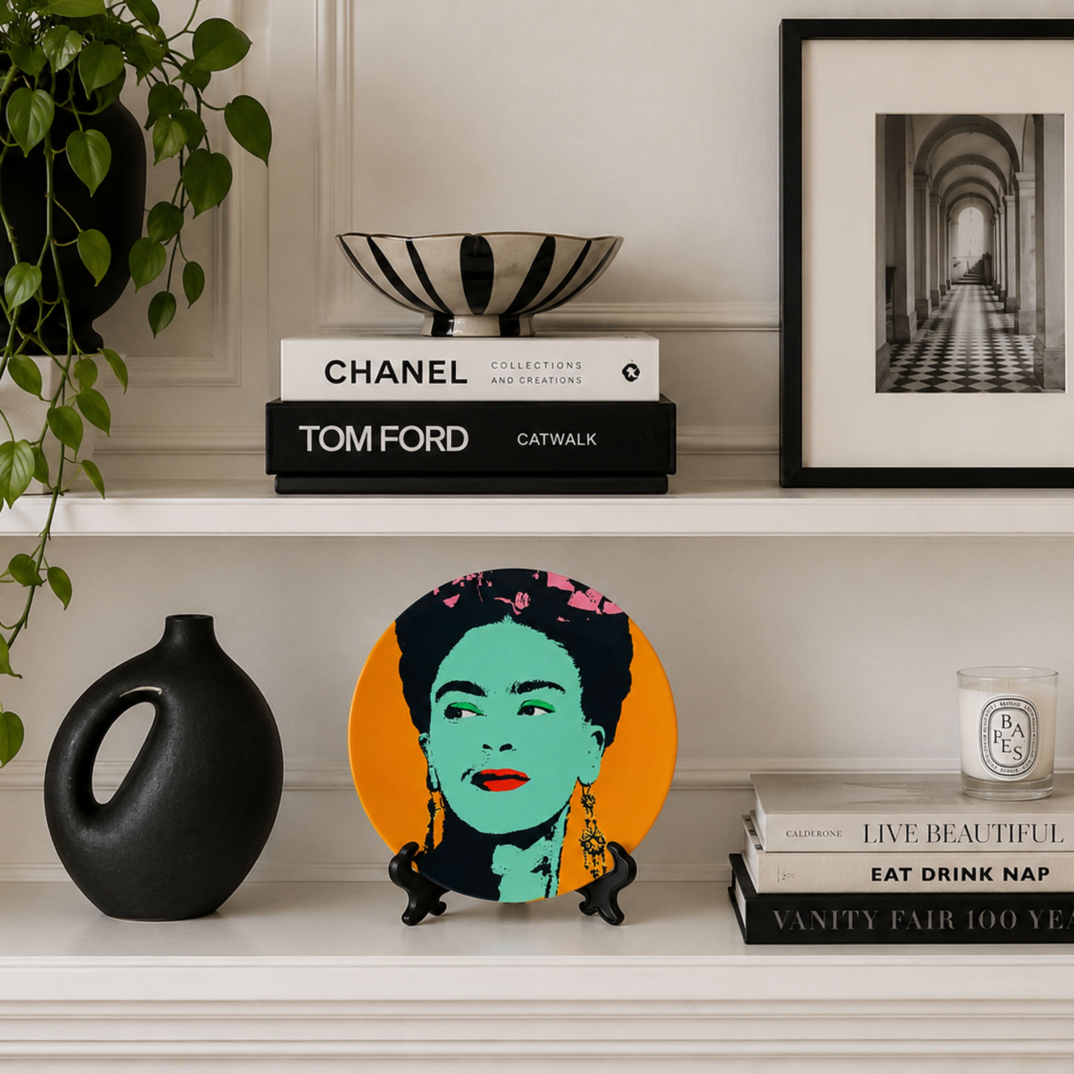 Pop art inspired Frida Kahlo decorative plate styled on white shelving with fashion books, black ceramic vase and monochrome framed artwork