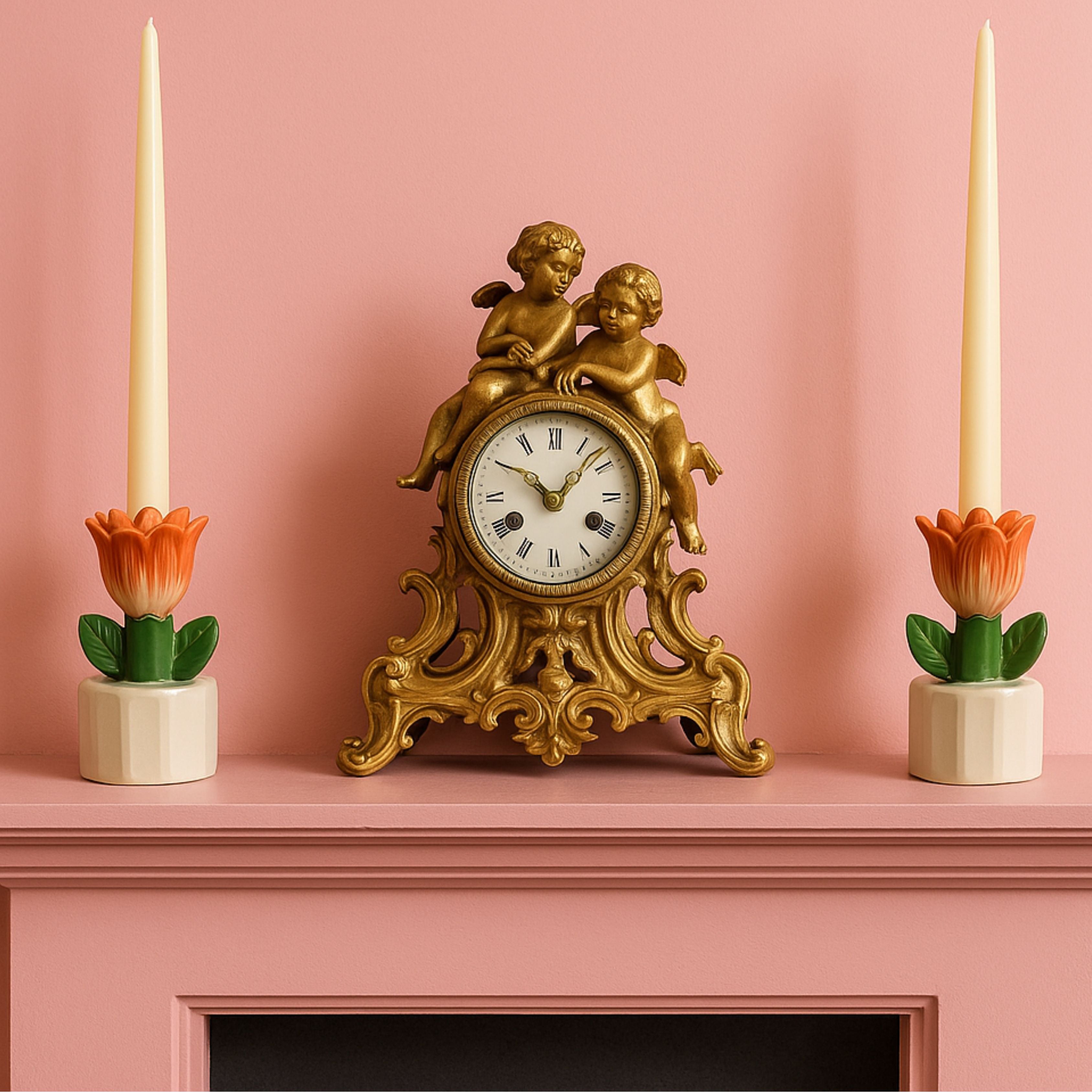 Tulip-shaped stoneware candle holders with tall taper candles styled on a pink fireplace mantel alongside an ornate gold cherub clock.