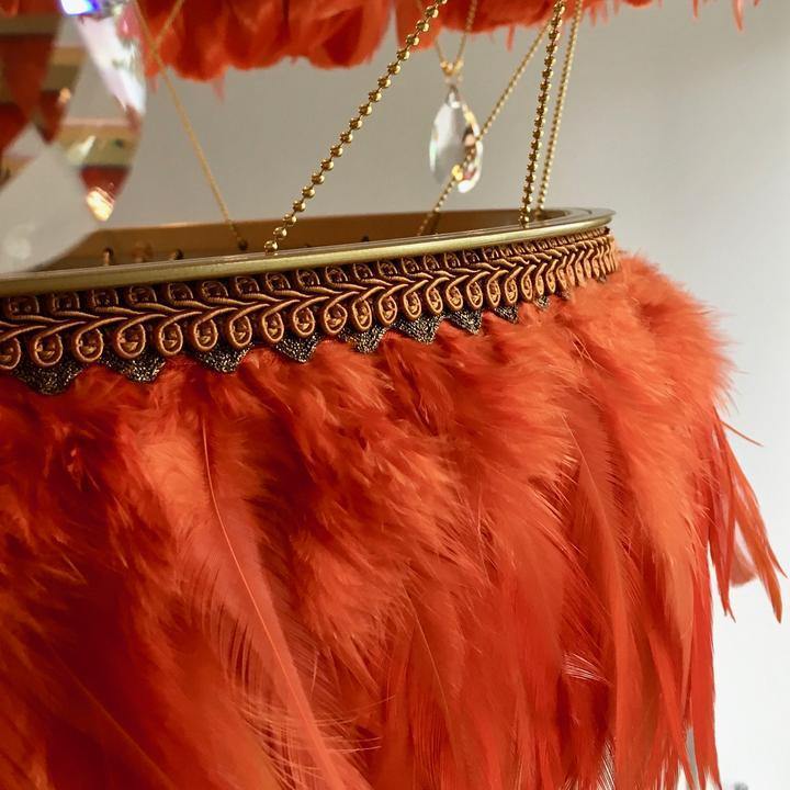Close-up of burnt orange Bertie feather light shade showing decorative trim, gold chain supports, and crystal drop detail