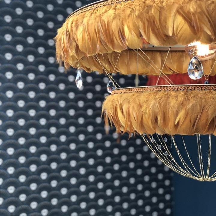 Close-up of mustard yellow Bertie two-tier feather light shade with crystal drops, shown against a blue patterned wall