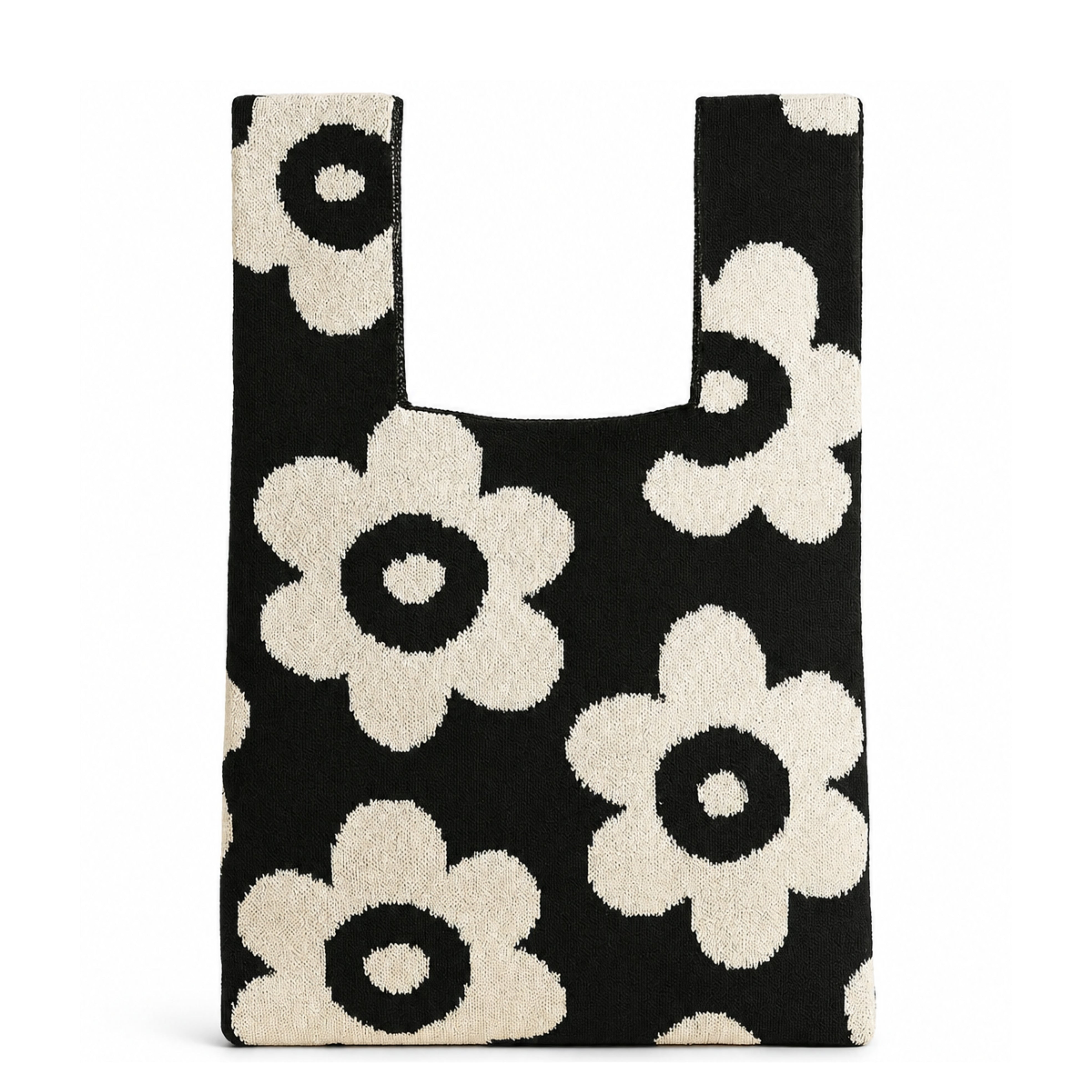 Black knitted tote bag featuring oversized cream floral motifs on a classic black background, photographed against a clean white background with a soft natural shadow beneath the bag.