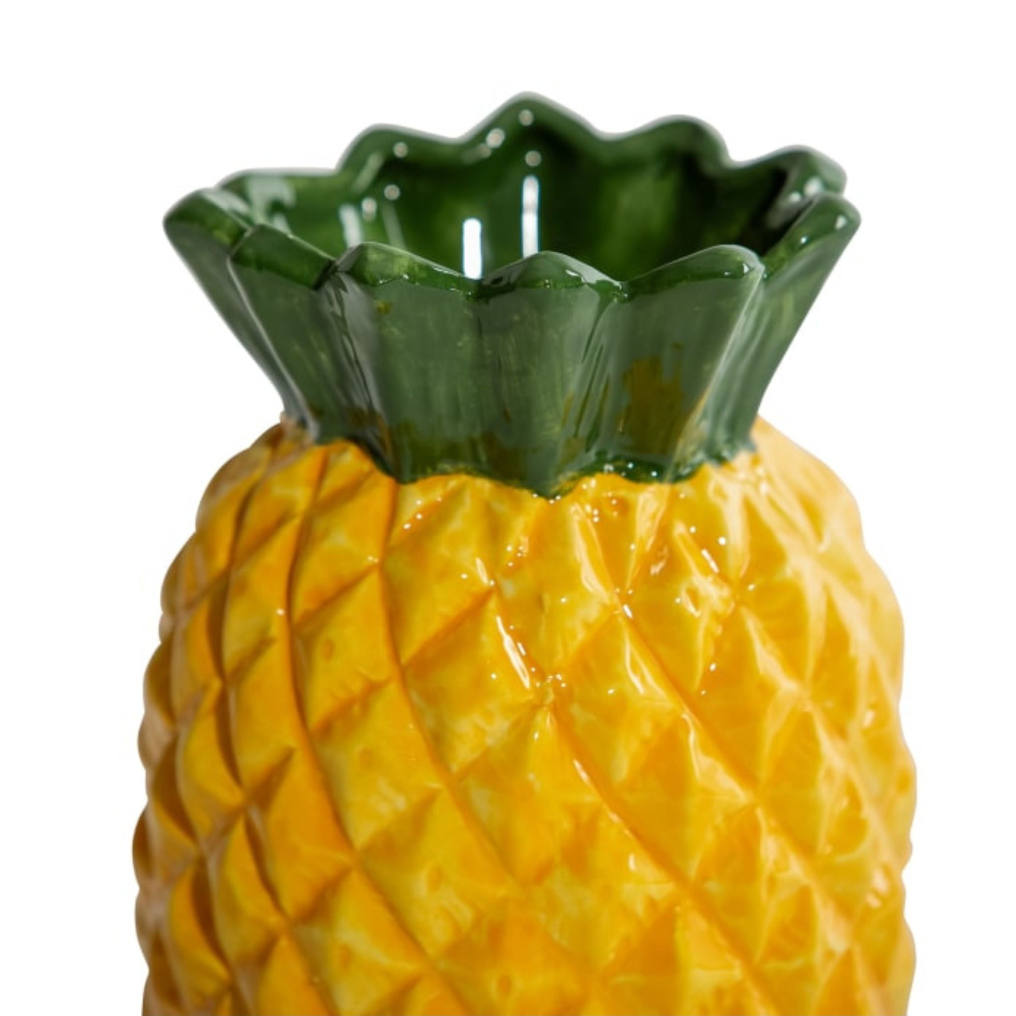 Close-up of ceramic pineapple vase with glossy yellow textured body and green leaf top on white background