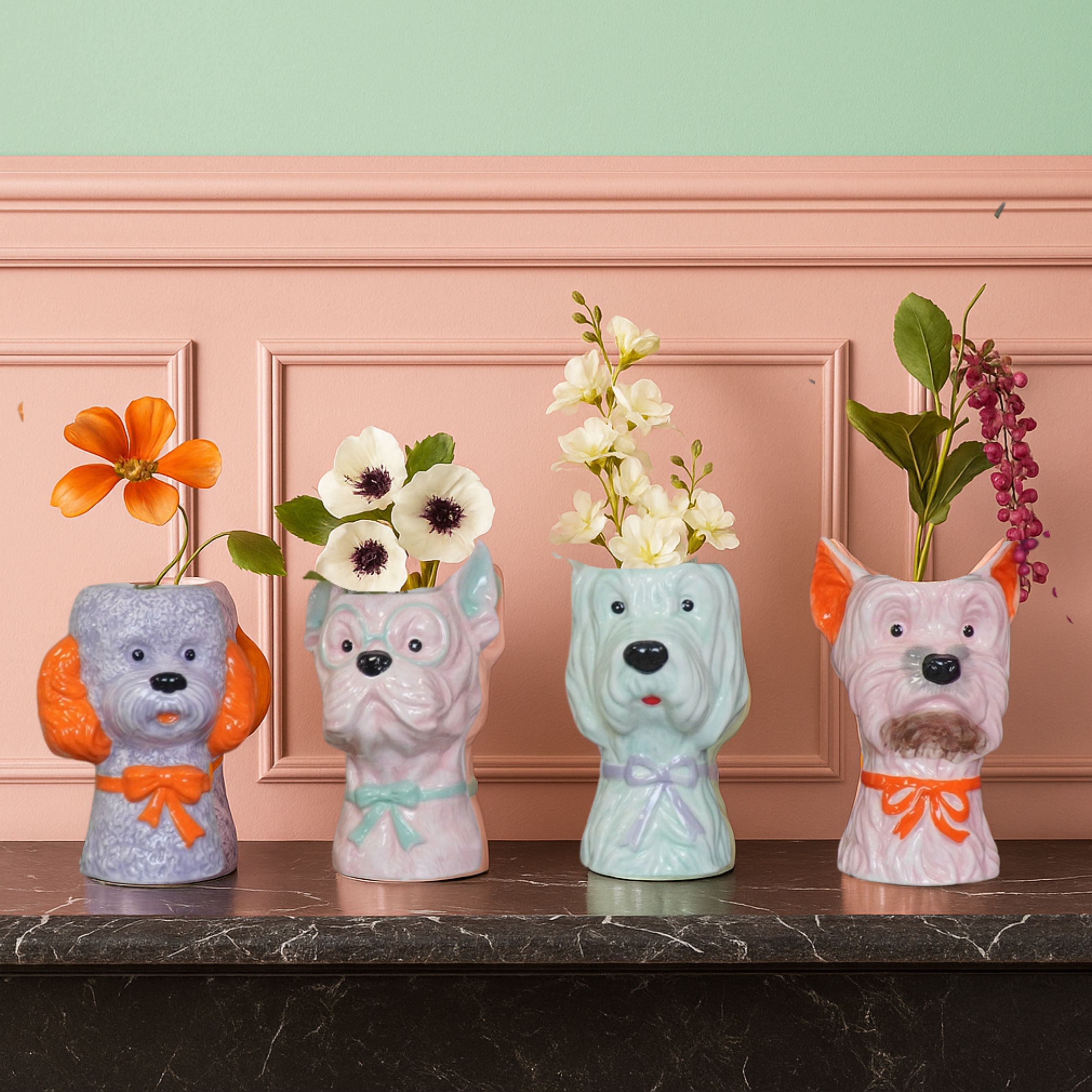 Four colourful dog-shaped ceramic vases filled with flowers, displayed on a dark marble surface against a peach panelled wall.