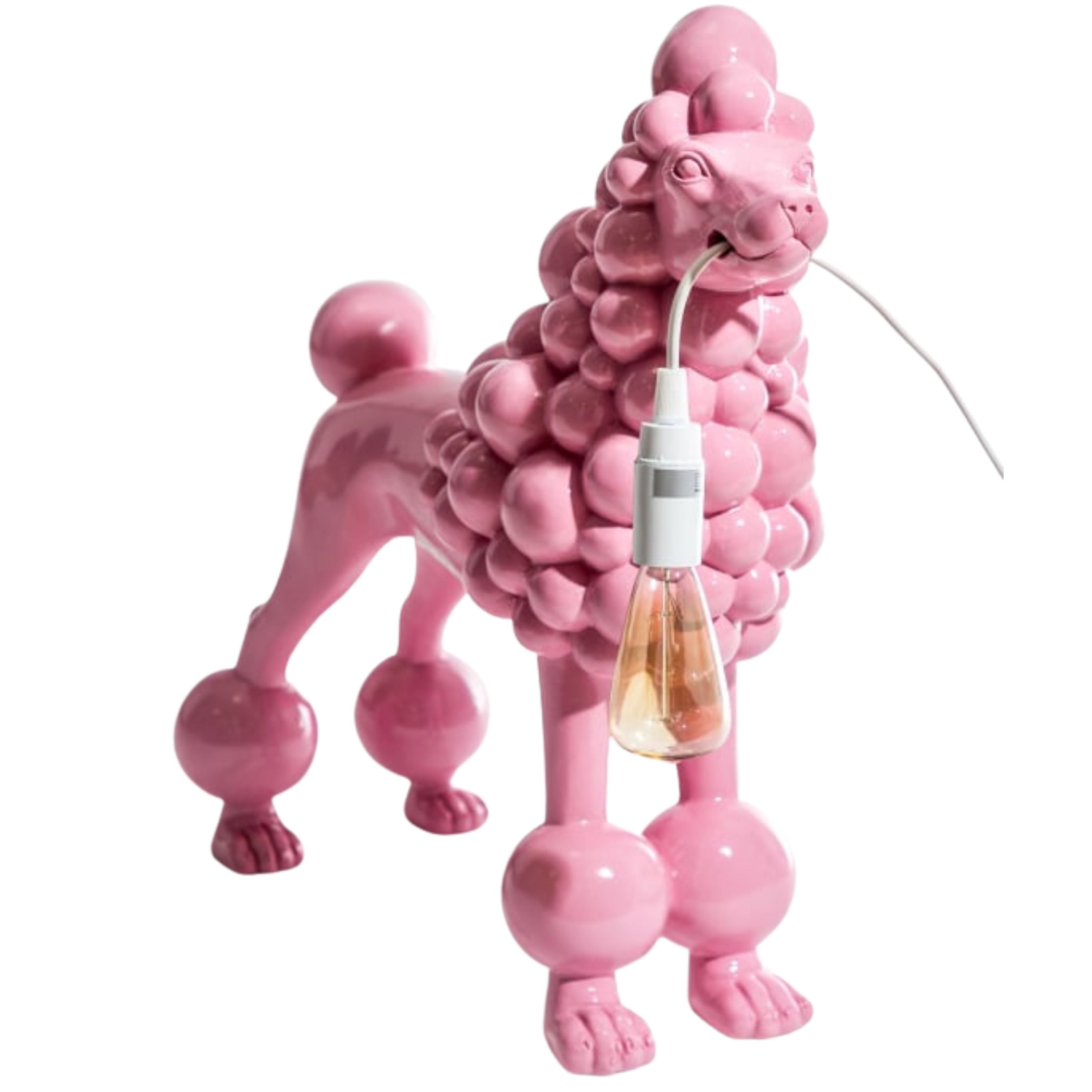 Glossy pink resin poodle lamp standing on four legs, holding a bulb in its mouth, photographed on a white background