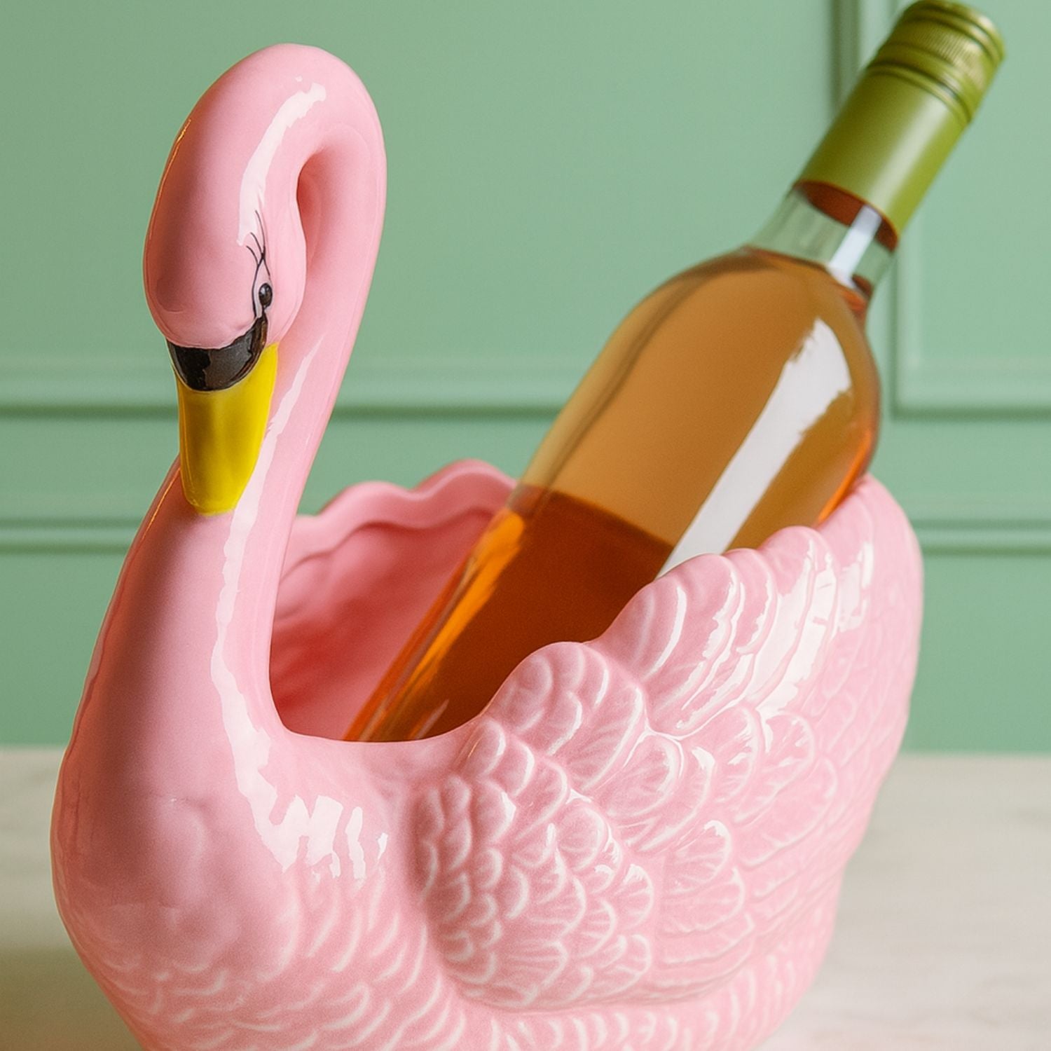 Glossy pink swan ceramic planter holding a bottle of rosé wine against a mint green background, playful home decor by Lizzie Onion’s Emporium.