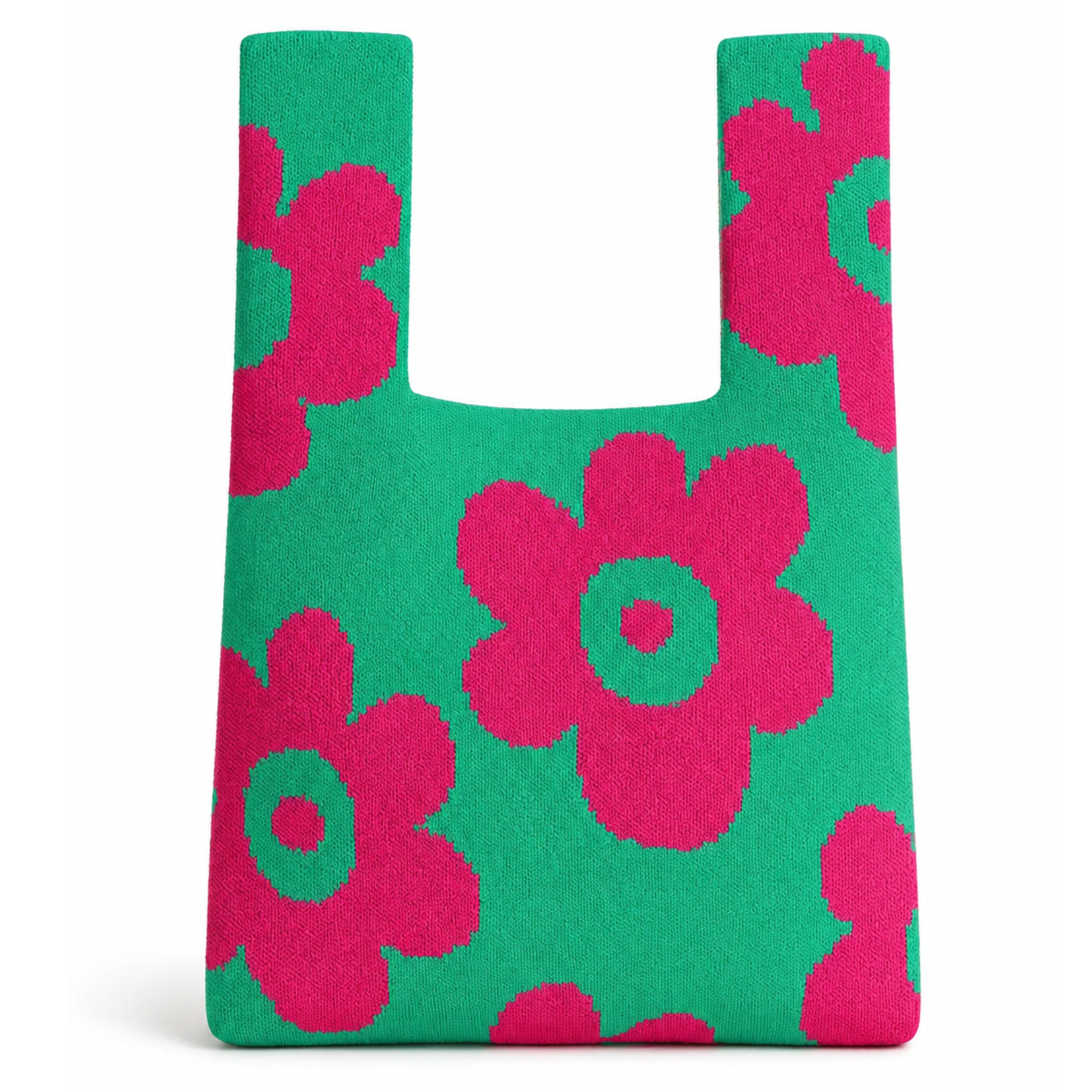 Green knitted tote bag featuring oversized hot pink floral motifs on a vibrant green background, photographed against a clean white background with a soft natural shadow beneath the bag.