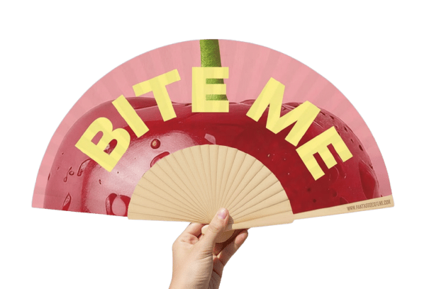 Hand holding a pink cherry print folding fan with bold 'BITE ME' slogan and natural wooden frame.