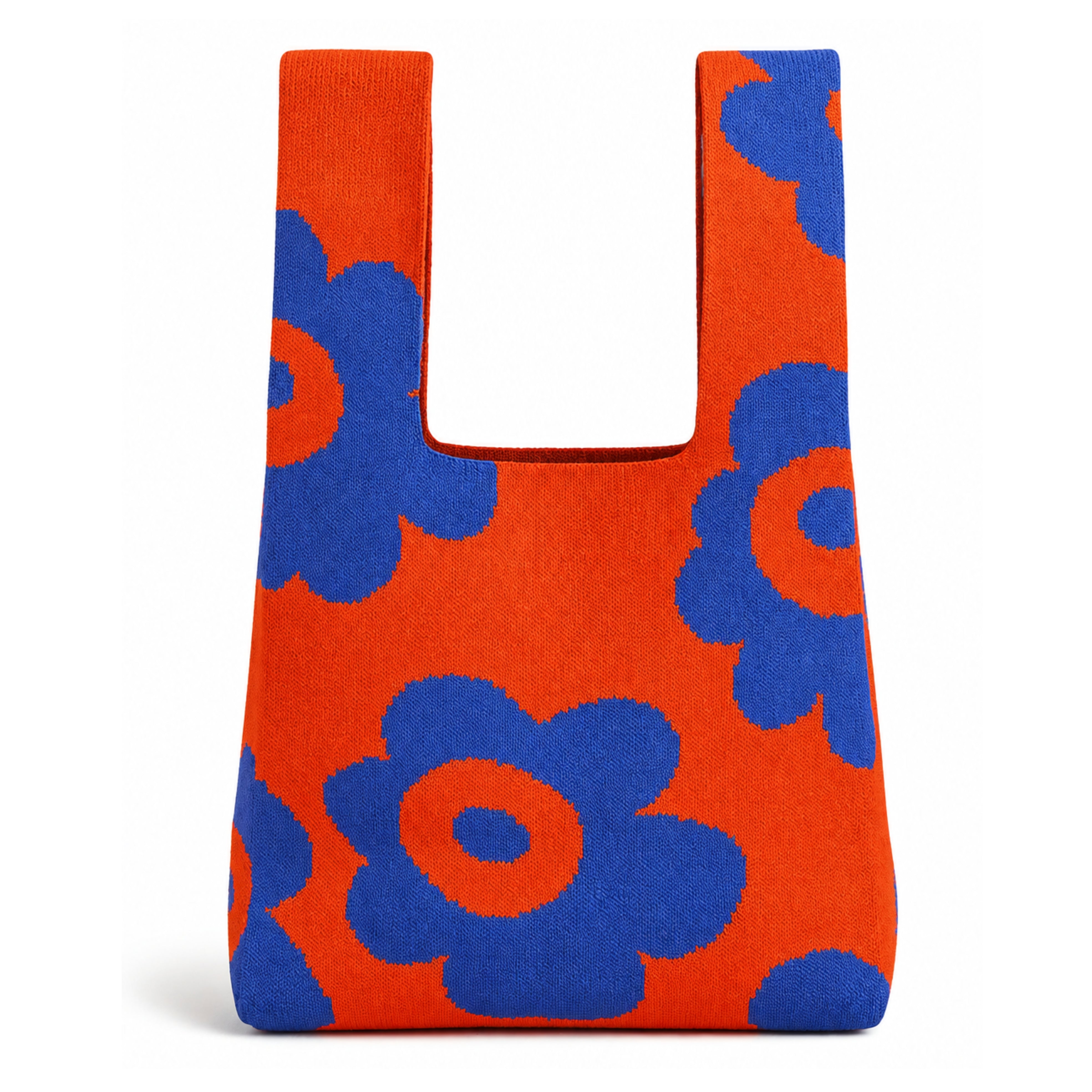 Orange and blue knitted tote bag featuring oversized blue floral motifs on a vibrant orange background, photographed against a clean white background with a soft natural shadow beneath the bag.