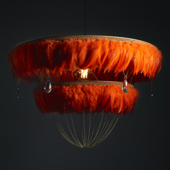 Burnt orange two-tier Bertie feather light shade with crystal drops softly glowing against a dark background.